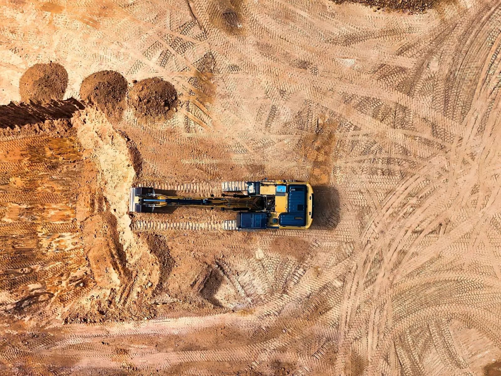 An excavator working a large graded site, seen from above